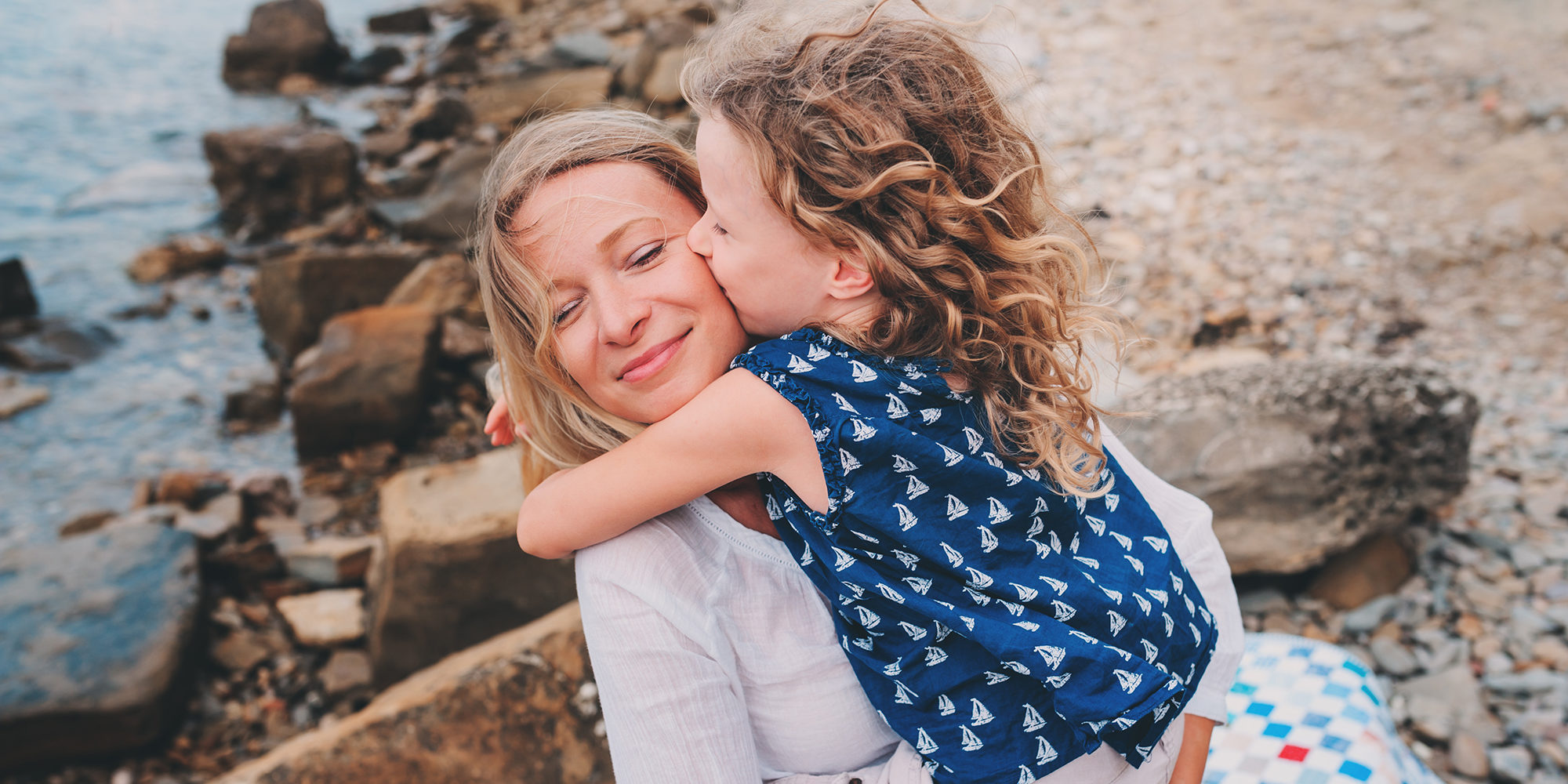 portrait of happy mother and daughter spending time together on the beach on summer vacation. Happy family traveling, cozy mood. Child kissing mother.